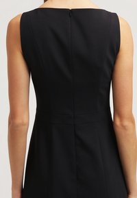 Vestido negro con un corsé ajustado, escote amplio y costura trasera recta, con cremallera oculta en la parte posterior. Textura de tejido suave.