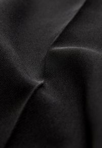 Gros plan d'un tissu noir lisse avec des plis subtils et une texture tissée fine visible sous un éclairage doux.