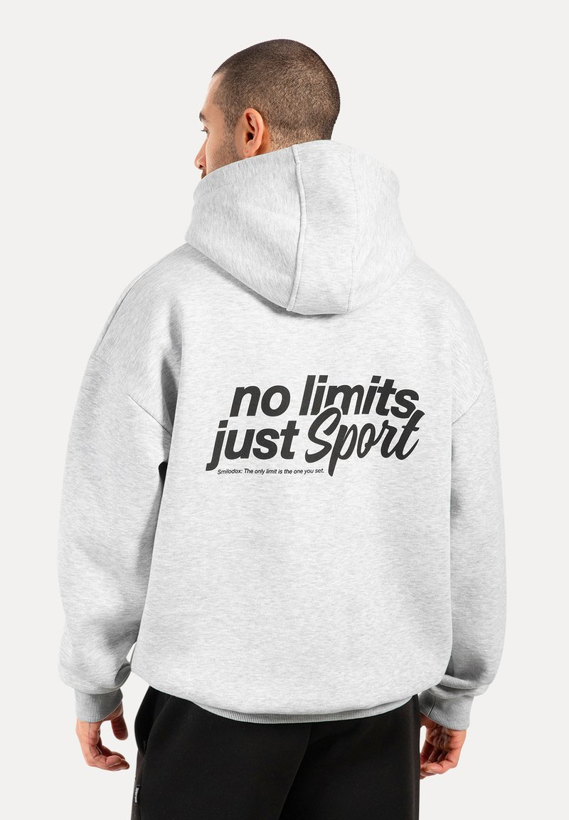 Felpa grigia oversize con cappuccio regolabile. Sul retro c'è una grande scritta nera: "no limits just Sport" con una citazione più piccola sotto.