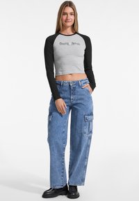 Gray cropped long-sleeve shirt with black sleeves, featuring "Guess Jeans" text, paired with blue cargo jeans and black ankle boots.