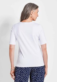 Weißes kurzärmliges Oberteil mit Rundhalsausschnitt, glatter Textur und figurbetontem Schnitt, kombiniert mit navyblauen Hosen mit Punkten.