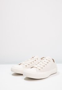 Baskets en toile beige avec œillets dorés, embout en caoutchouc et semelle texturée en caoutchouc. Design bas avec système de laçage.