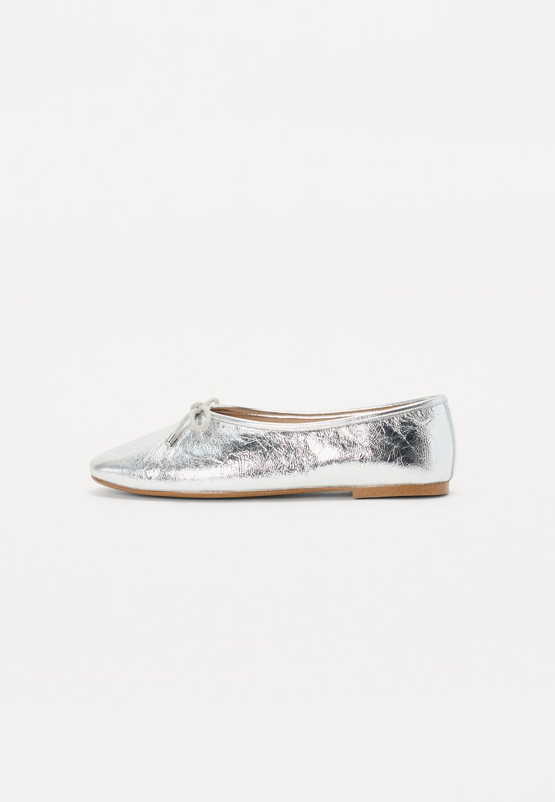 Ballerines argentées avec une finition métallique, présentant un bout arrondi et un nœud décoratif à l'avant. Semelle plate, design minimal.