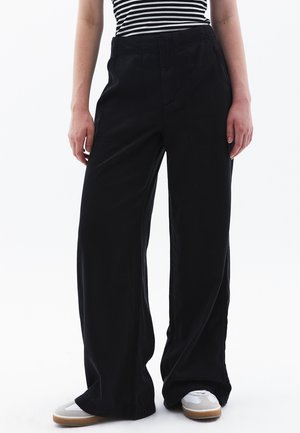 Pantalones negros de pierna ancha hechos de tejido ligero. Presentan una cintura alta, bolsillos frontales y una textura suave. Combinados con zapatillas blancas.