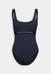 Costume da bagno intero blu navy con spalline larghe e scollatura a barchetta. Presenta una vita nera con logo e contrasti bianchi e rossi.