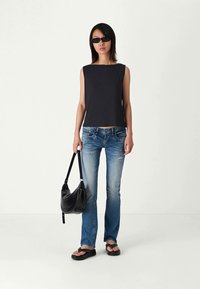 Top negro de canalé sin mangas, vaqueros azules con detalles desgastados, bolso negro de forma curva y chanclas negras.