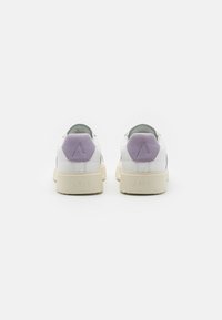Zapatillas blancas con acentos de ante púrpura claro, acabado de piel suave y suela beige texturizada. Presentan un logo hexagonal en el talón.