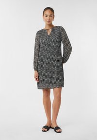 Zwart-witte jurk met een patroon, lange mouwen, een geplooide rok en een sleutelgat-halslijn. Gemaakt in combinatie met platte zwarte sandalen.