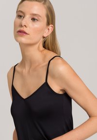 Camisola nera con spalline sottili, caratterizzata da un design a V e bordo scallop lungo il colletto. Tessuto liscio con una forma aderente.