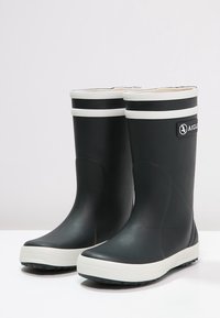 Bottes de pluie en caoutchouc noires avec une bande blanche en haut et une semelle blanche. Semelle texturée pour une bonne adhérence. Logo Aigle sur le côté.
