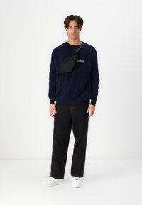 Mørkeblå mønstret sweater med en sort crossbody taske, parret med sorte bukser og hvide sneakers, som har en afslappet pasform og struktureret stof.