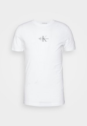 Hvid bomulds-T-shirt med korte ærmer og rund halsudskæring. Har en grå "CK"-logo trykt på forsiden. Glat tekstur.