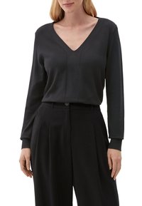 Schwarzer V-Ausschnitt-Pullover mit langen Ärmeln, glatter Textur und genähten Details auf der Vorderseite, kombiniert mit schwarzen Plisseehosen.