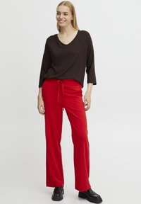 Red wide-leg pants with a drawstring waistband, paired with a loose-fitting brown top featuring a V-neck and three-quarter sleeves.