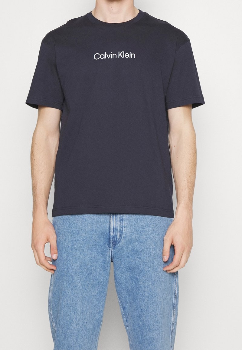 Námořnicky modré bavlněné tričko, krátké rukávy, kulatý výstřih, se středovým bílým logem "Calvin Klein" na hrudi. Volný střih.