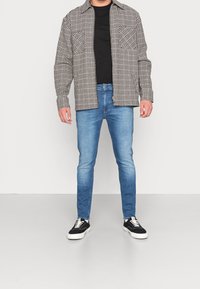 Černobílá kockovaná košile se dvěma náprsními kapsami, zkombinovaná se světle modrými slim-fit džíny a černými teniskami s bílou podrážkou.