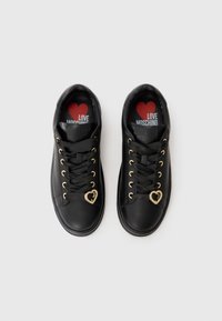Black leather sneakers with gold hardware, heart-shaped accents, and black laces. Red and white printed insoles feature a heart design.