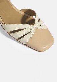 Beige en crèmekleurige leren sandaal met een vierkante teen, voorzien van uitgehouwen banden en een soepele, gestructureerde afwerking.