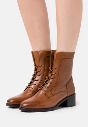 Braune Lederstiefeletten mit Schnürdesign, Blockabsatz und Steppnähten an den Seiten und an der Spitze. Glatte Textur, minimalistische Akzente.