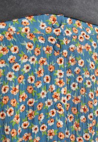Blått blommigt tyg med orangea och vita blommor, med en strukturerad yta och två knappar längs midjebandet.