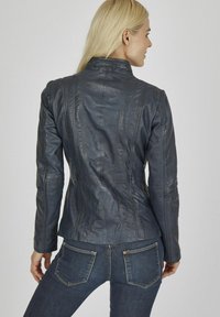 Dunkelblaue Lederjacke mit tailliertem Design, sichtbaren Nähten, stehem Kragen und langen Ärmeln, kombiniert mit dunklen Jeans.