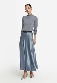 Haut gris à manches longues avec un col haut, associé à une jupe longue en satin bleu clair fluide, accentuée par une ceinture noire et des talons argentés.