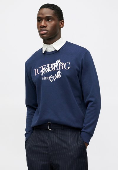 Σκούφος ναυτικού μπλε χρώματος με ραμμένα μανίκια και λαιμόκοψη. Περιέχει λευκό κείμενο με μοτίβο από επικάλυψη: "ICEBERG since CLUB" σε γραφιστικό σχέδιο.