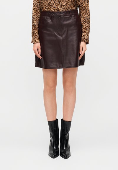 Jupe en cuir marron au design ajusté, dotée de deux poches avant et d'une coupe droite, associée à des bottines noires.