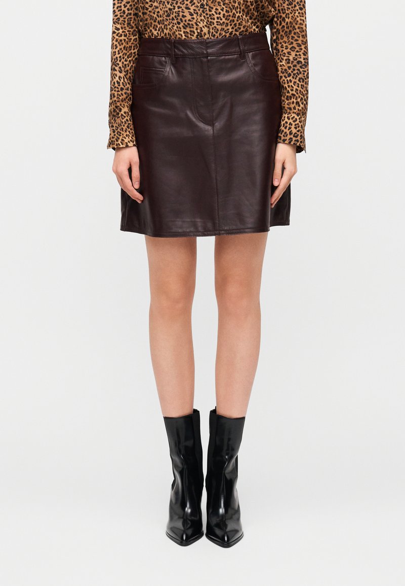 Καφέ δερμάτινη φούστα με εφαρμοστή σχεδίαση, που διαθέτει δύο μπροστινές τσέπες και ίσια γραμμή, συνδυασμένη με μαύρα μποτάκια μέχρι τον αστράγαλο.