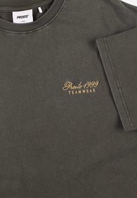 Ciemnoszara bawełniana koszulka z okrągłym dekoltem, krótkimi rękawami oraz złotym haftem na piersi z napisem "Prosto 1999 TEAMWEAR".