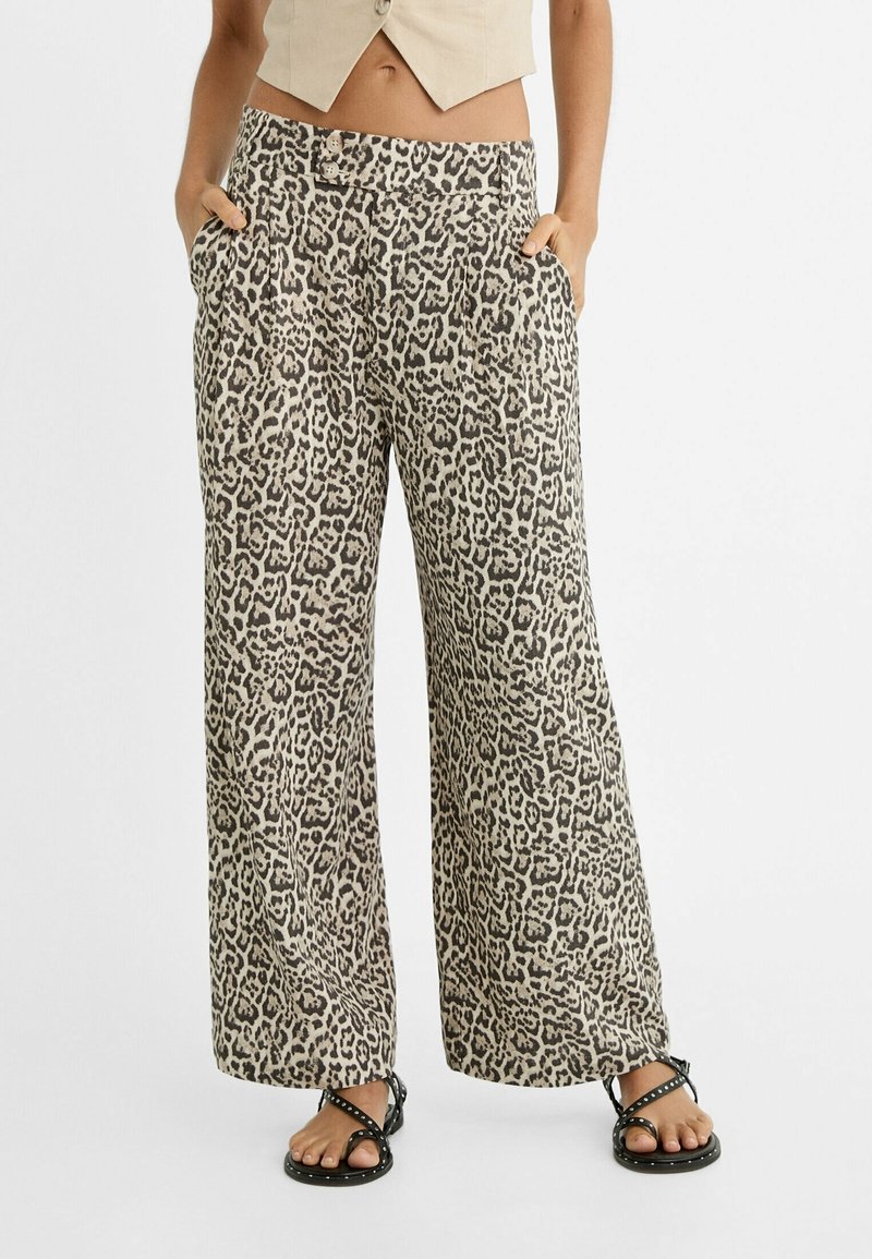 Pantalon à jambes larges avec imprimé léopard beige et noir, porté avec des sandales noires à clous et un top beige court, mains dans les poches.