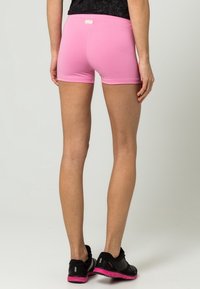 Różowe bawełniane szorty o gładkiej fakturze, dopasowanym kroju i małej metce z tyłu. Noszone z czarnymi butami sportowymi z różowymi akcentami.