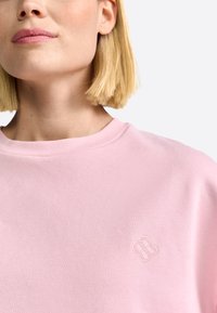 Roze sweatshirt met een ribbelboord bij de ronde hals en een klein geborduurd bloemlogo op de borst. Zacht, glad stof, casual pasvorm.