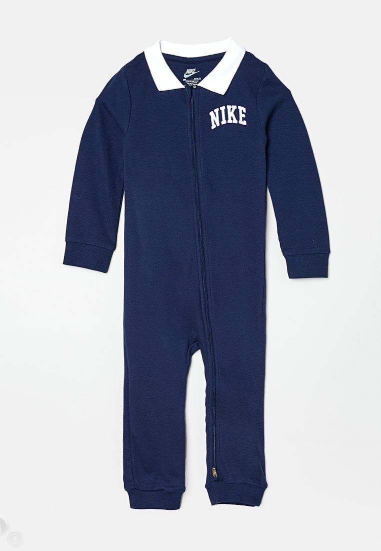 Combinaison à zip bleu marine avec des manches longues, un col blanc et le logo Nike sur la poitrine. Tissu doux avec des poignets et des chevilles ajustés.