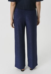 Weite Hosen aus einem strukturierten, dunkelblauen Stoff mit einem subtilen Schimmer. Sie verfügen über eine hohe Taille und einen nahtlosen Abschluss am Saum.