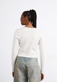 Light gray ribbed long-sleeve top with a square neckline, paired with faded blue denim jeans featuring back pockets. Textured fabric detail visible.