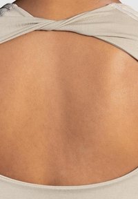 Haut en tissu beige avec un grand dos nu, arborant un design torsadé au niveau du cou, une texture douce et un léger éclat.