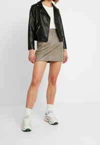 Černá kožená motorkářská bunda, bílý tričko, mini sukně z olivově zelené umělé semiše a masivní bílé tenisky s  černými a zelenými akcenty.