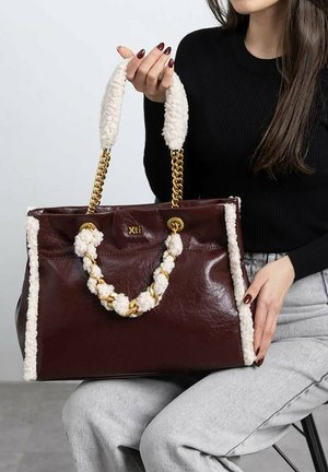 Bolso tote de cuero burdeos oscuro con detalles de piel crema, correas de cadena trenzada y herrajes dorados. Presenta un logo en el frente.