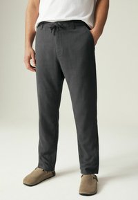 Pantalons légers, gris foncé, avec une taille à cordon de serrage et des poches latérales, associés à des chaussures en suède marron à enfiler. Tissu lisse et respirant.