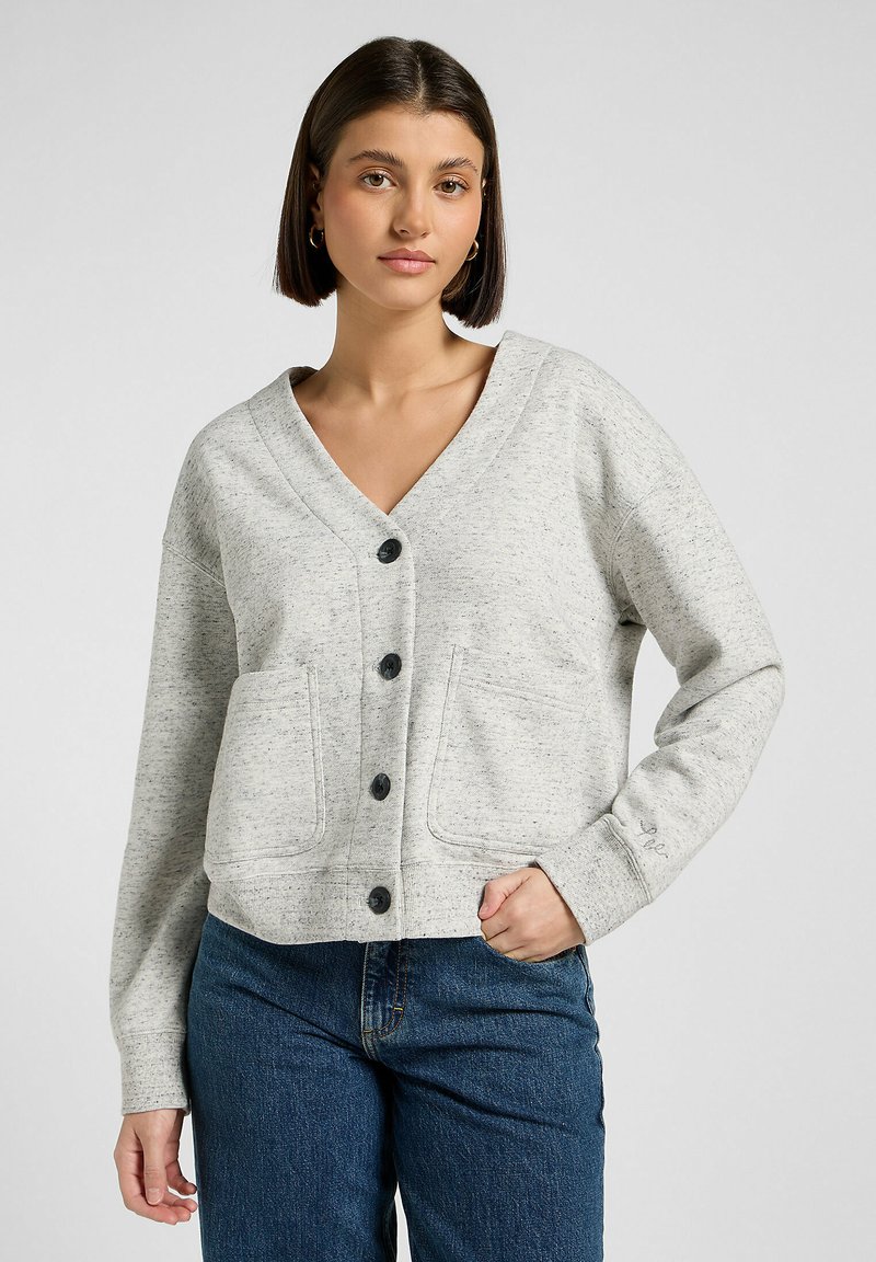 Grå knapplös cardigan med V-ringning, som har två framfickor och ett texturerat stickat mönster. Matcher med blå jeans.