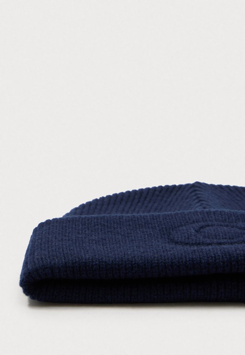 Berretto di maglia blu navy con texture a coste, ripiegato al polsino, caratterizzato da un motivo logo impresso sul tessuto.