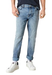 Jeans de mezclilla azul claro con un corte relajado, puños enrollados, cinco bolsillos y cierre frontal de botón. Combinados con zapatillas blanca.