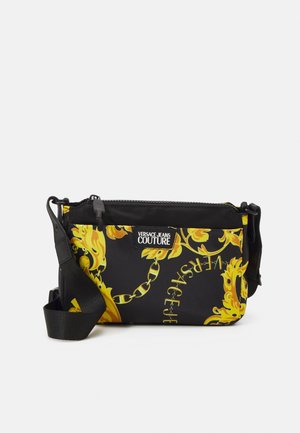 Bolso bandolera negro con cadena amarilla ornamentada y patrón de hojas, correa ajustable y etiqueta frontal "Versace Jeans Couture".