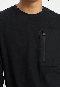 Suéter negro de manga larga con un patrón texturizado, que cuenta con un bolsillo en el pecho con cremallera y un cuello redondo. Tela suave con un corte casual.