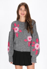 Grå tröja av ett luddigt material, prydd med stora rosa blommiga broderier på ärmarna, med en avslappnad passform och ribbade manschetter.