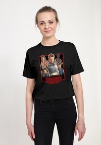 Zwart katoenen T-shirt met een gedrukte afbeelding uit "Stranger Things," met meerdere personages binnen een rood kader.
