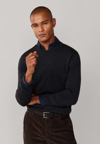 Tmavě šedý pletený svetr s kulatým výstřihem, vrstvený přes modrou košilovou košili. Spárujte s hnědými kordovými kalhotami a černým pásem.