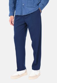 Pantaloni blu navy realizzati in un tessuto liscio, con una vestibilità comoda e dettagli delle pieghe. Abbinati a sneakers bianche con accenti beige.