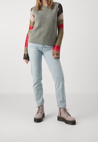 Grå stickad tröja med flerfärgade texturerade ärmar; ljusblå jeans; snörda rosa stövlar med svarta sulor.